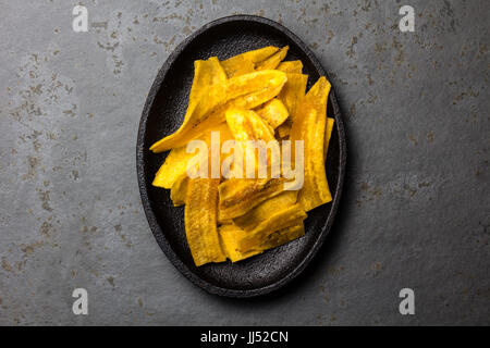 Gesunde hausgemachte Wegerich Bananenchips auf schwarzem Teller, Schiefer Hintergrund. Stockfoto