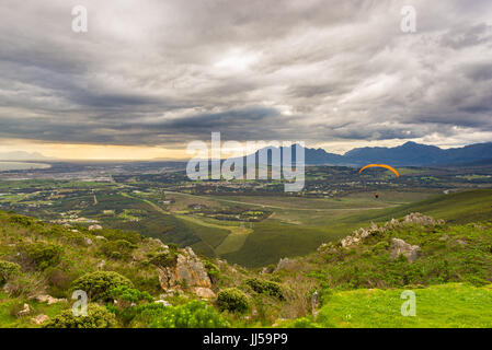 Gleitschirm fliegen über die grünen Berge rund um Cape Town, Südafrika. Wintersaison, bewölkt und dramatischen Himmel. Nicht erkennbare Personen. Stockfoto