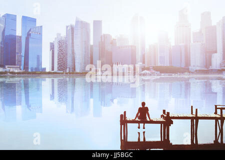 Traum Konzept, Mann auf dem Steg sitzen und genießen Sie modernen Stadtbild Skyline Blick