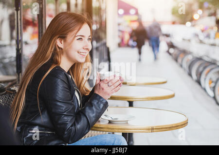 Glücklich lächelnde attraktive junge Frau mit Tasse Kaffee in Street Cafe in Europa, hübsches Mädchen in Paris. Stockfoto