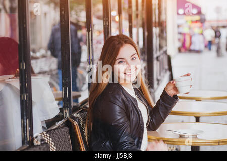 Glücklich lächelnde Frau trinkt Kaffee in Straßencafés und auf Kamera, gute Laune Stockfoto