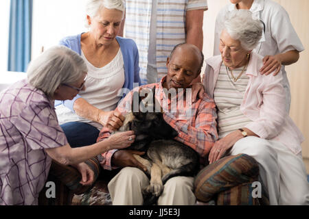 Ältere Leute mit Arzt streicheln Hund auf Couch im Pflegeheim Stockfoto