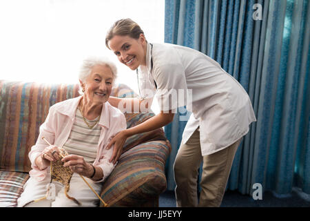 Porträt von lächelnden senior Frau mit Stricken mit Ärztin gegen Fenster im Altersheim Stockfoto