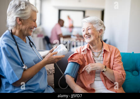 Lächelnde ältere Frau im Gespräch mit der Ärztin während der Blutdruck-Check-up im Pflegeheim Stockfoto