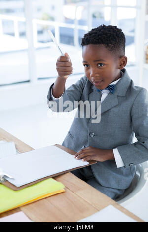 Geschäftsmann hält Stift sitzend auf Stuhl am Schreibtisch im Büro Stockfoto