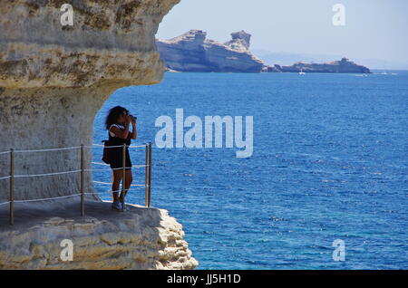 Weibliche Touristen zu Fuß auf eine Passage in den Klippen nahe dem Meeresspiegel, unterhalb der mittelalterlichen Burg von Bonifacio gehauen. Stockfoto