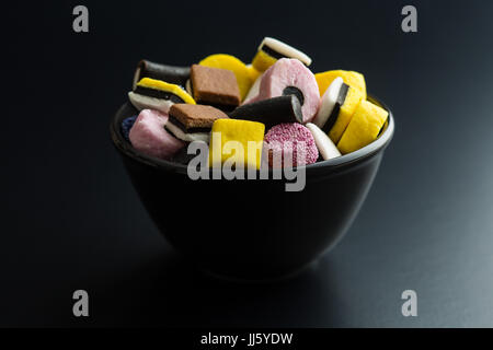 Gemischte Lakritz-Bonbons in schwarz Schüssel auf schwarzem Hintergrund. Stockfoto