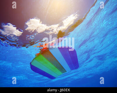 Regenbogen Muster Styropor schwimmen Board oder Fußleiste im Schwimmbadwasser, Sommer Urlaub Freizeitaktivität Objekt in der poolsid Stockfoto