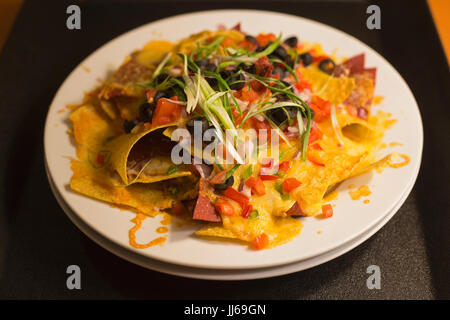 Teller mit Nachos: knusprige Tortillachips, erhitzt mit geschmolzenem Käse, schwarzen Oliven, grünen Zwiebeln, roten Paprika, grünen Paprika und Tomaten Stockfoto