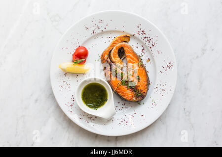 Lachssteak mit Kräutern, Zitrone, Tomaten-Salsa-Sauce auf einem Teller. Ansicht von oben Stockfoto