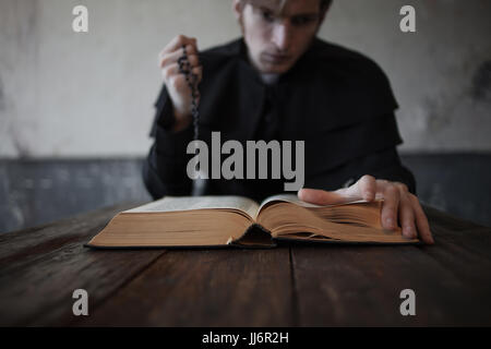 Seite der Bibel, close-up. Porträt von hübschen jungen katholischen Priester. Die Hand im Fokus Stockfoto