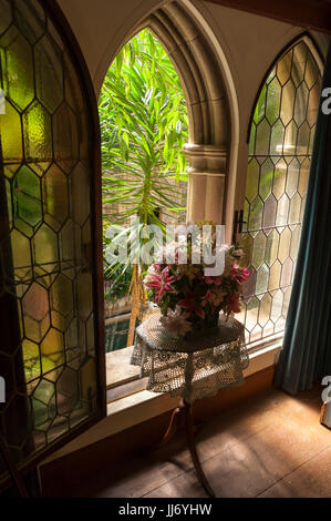 Vase mit Lilien auf einem dreibeinigen Tisch, vor einem offenen Fenster Bleiglasfenstern, Aufsicht über ein Innenhof, an Hammond Castle, in Gloucester, MA Stockfoto