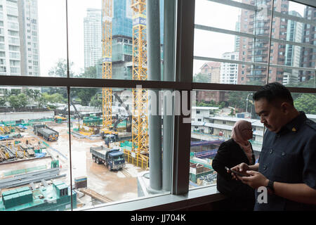 Eine Baustelle ist durch ein Fenster gesehen, wie ein Mann am Telefon im Kuala Lumpur Convention Center in Kuala Lumpur, Malaysia spricht Stockfoto