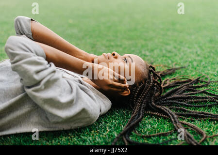 Musik im Kopfhörer hört die schöne afroamerikanischen Sportgirl während der Verlegung auf dem Rasen. Das Close-up Seite Porträt. Stockfoto