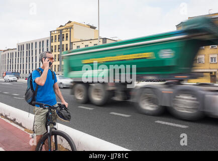 Männliche Radfahrer auf dem Radweg entlang der viel befahrenen Straße, telefonieren mit Handy. Stockfoto