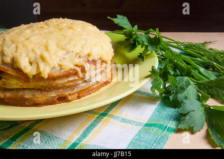 Pfannkuchen Sie-Torte mit Champignons und Hühnerfleisch, überbacken mit Käse auf grüne Platte. Pfannkuchen-Kuchen auf Teller mit Kräutern grün: grüne Zwiebel, Dill, Petersilie Arou Stockfoto