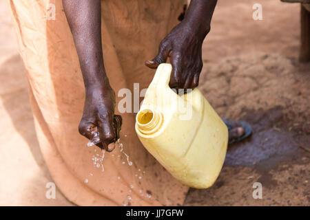 Eine alte Afrikanische Frau gießt Wasser über ihre Hand aus einem gelben Kanister. Stockfoto