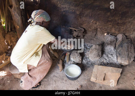 Eine alte schwarze ugandischen Frau Kochen in Metall Töpfe auf Kohlenfeuer in einer primitiven Außenküche in Buikwe, Uganda im Juli 2017 Stockfoto