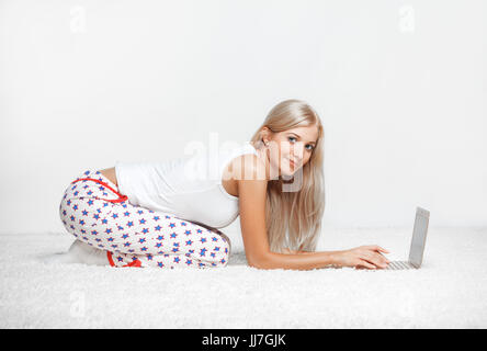 Junge blonde Frau im Schlafanzug auf weißen Laptop Surfen gesamte-Teppich sitzen Stockfoto