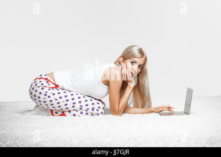 Junge blonde Frau im Schlafanzug auf weißen Laptop Surfen gesamte-Teppich sitzen Stockfoto