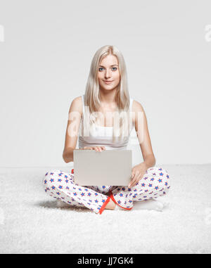 Junge blonde Frau im Schlafanzug auf weißen Laptop Surfen gesamte-Teppich sitzen Stockfoto