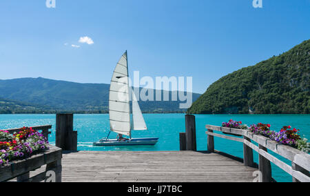 Ein schönes weißes Boot segelt vorbei an einem hölzernen Dock am Lac d ' Annecy im Süden Frankreichs. Stockfoto