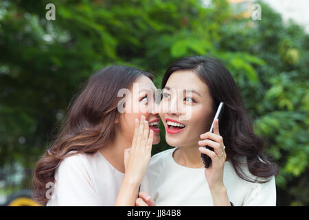 Surpried junge Frau Flüstern bei einem fröhlichen Freund während auf Abruf Stockfoto