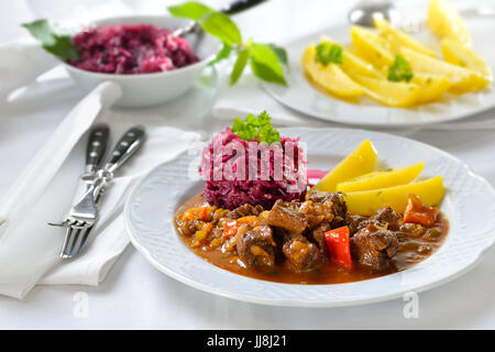 Heißes ungarisches Gulasch serviert mit gebutterten Petersilienkartoffeln und Rotkohl Stockfoto