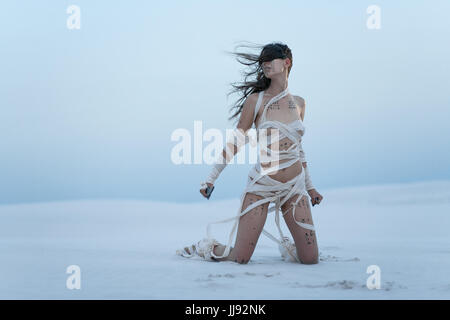 Mädchen in der Wüste in Bild der ägyptischen Mumie mit Messer in der Hand. Sie kniet, alle eingewickelt in Verbände und sie hat Hieroglyphen auf ihrem Körper. Stockfoto