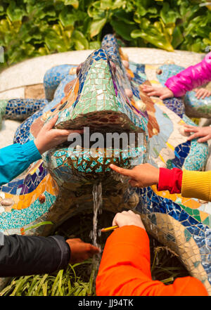 multi-ethnischen Grundschulkinder Hände berühren Gaudis berühmte Mosaik Drache Brunnen im Park Güell auf einem Schulausflug im Barcelo Stockfoto