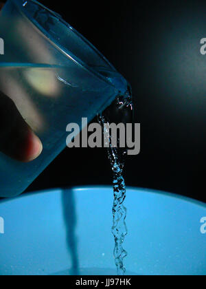 Wasser gegossen aus einem blassen blauen Glas mit schwarzem Hintergrund - in der Bewegung eingefroren Stockfoto