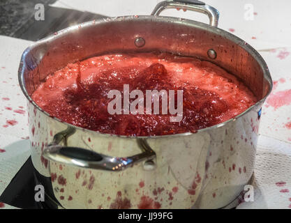 Himbeermarmelade energisch auf einem Induktionskochfeld in einem metallischen Topf kochen, bedeckt die Umgebung in Papier, um Spritzer zu vermeiden. Stockfoto