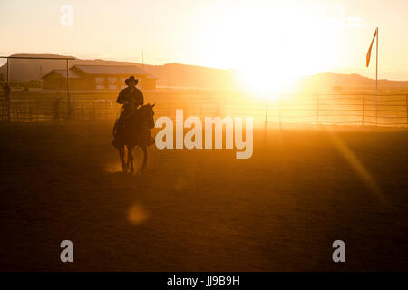 Ein Cowboy trabt auf seinem Pferd bei Sonnenuntergang bei einem Rodeo in Utah. Stockfoto