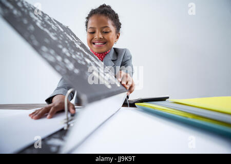 Lächelndes Mädchen vorgibt als Geschäftsfrau arbeiten am Schreibtisch vor weißem Hintergrund Stockfoto