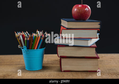 Apple auf Buch Stapel mit Farbstiften auf Tisch vor schwarzem Hintergrund Stockfoto