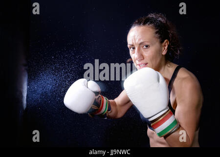 Eine Boxer Frau wirft einen Schlag in der Plünderung. Spritzer von Wasser und Schweiß auf dem schwarzen Hintergrund. Stockfoto