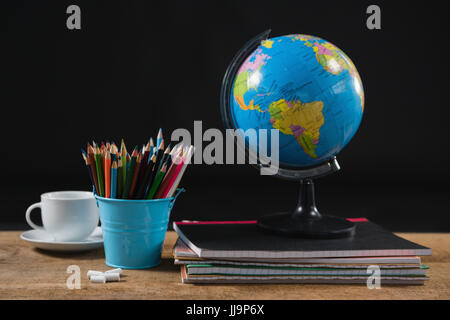 Verschiedene Schulsachen und Globus auf Tisch vor schwarzem Hintergrund Stockfoto