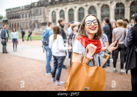 Lächelnde Mädchen fotografieren mit Smartphone während des Besuchs mit Reisegruppe des alten Palastes in Dresden City, Deutschland Stockfoto