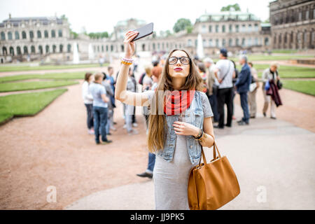 Lächelnde Mädchen fotografieren mit Smartphone während des Besuchs mit Reisegruppe des alten Palastes in Dresden City, Deutschland Stockfoto