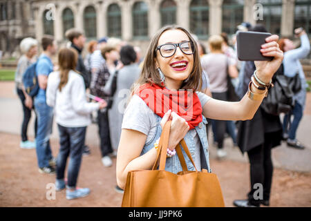 Lächelnde Mädchen fotografieren mit Smartphone während des Besuchs mit Reisegruppe des alten Palastes in Dresden City, Deutschland Stockfoto