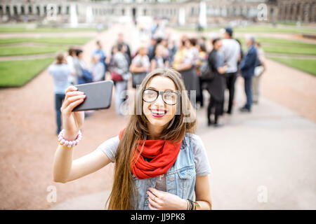 Lächelnde Mädchen fotografieren mit Smartphone während des Besuchs mit Reisegruppe des alten Palastes in Dresden City, Deutschland Stockfoto