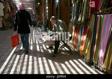 Ein Kaufmann liest die Zeitung in Marrakeschs Medina Viertel Stockfoto