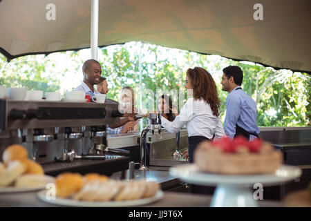 Kellnerin serviert Kaffee an Kunden am Schalter des Café im freien Stockfoto