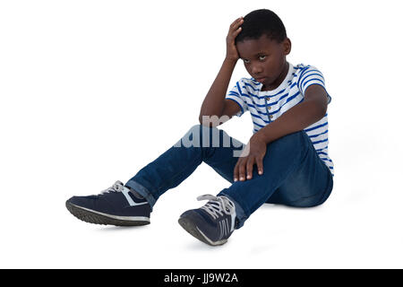 Traurige Junge sitzt mit Hand am Kopf vor weißem Hintergrund Stockfoto