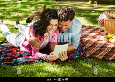 Paar auf der Picknickdecke liegen und mit digital-Tablette im park Stockfoto