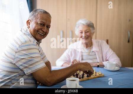 Lächelnd senior Mann spielt Schach mit Freund beim Sitzen am Tisch im Pflegeheim Stockfoto