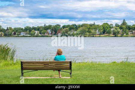 Frau sitzt auf einer Holzbank an einem See in Massachusetts Stockfoto