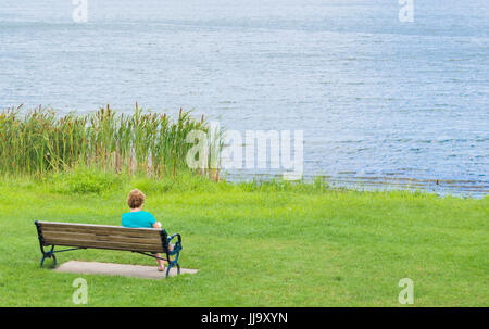 Frau sitzt auf einer Holzbank an einem See in Massachusetts Stockfoto