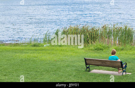 Frau sitzt auf einer Holzbank an einem See in Massachusetts Stockfoto