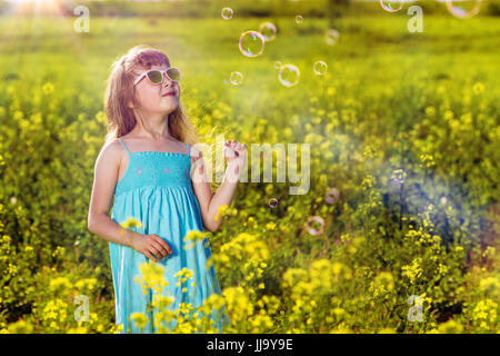 Mädchen in einem blauen Kleid in einem Feld. Gelbe Blüten im Sommer. Sonniger Morgen in der Natur. Stockfoto